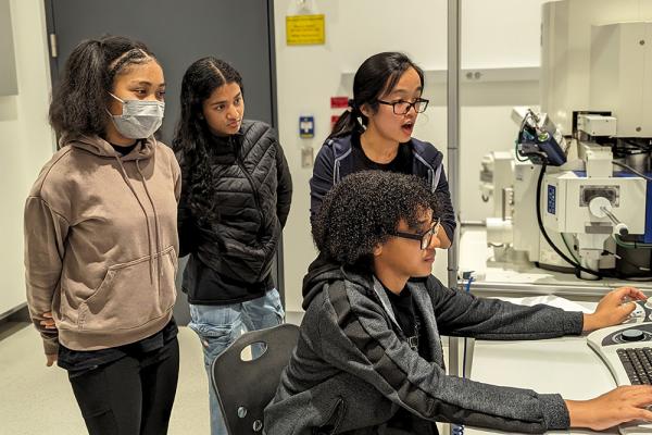 Middle schoolers in the MITES Saturdays science program at MIT examine images of material samples through a scanning electron microscope at MIT.nano, with the help of Rebecca Li (third from left), a postdoc in the Department of Materials Science and Engineering. The students participated in a pilot education program called EMERGE aimed at engaging students in hands-on scientific exploration.